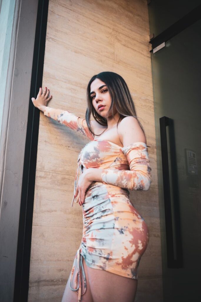 A stylish young woman in a trendy dress poses confidently against a modern building wall.