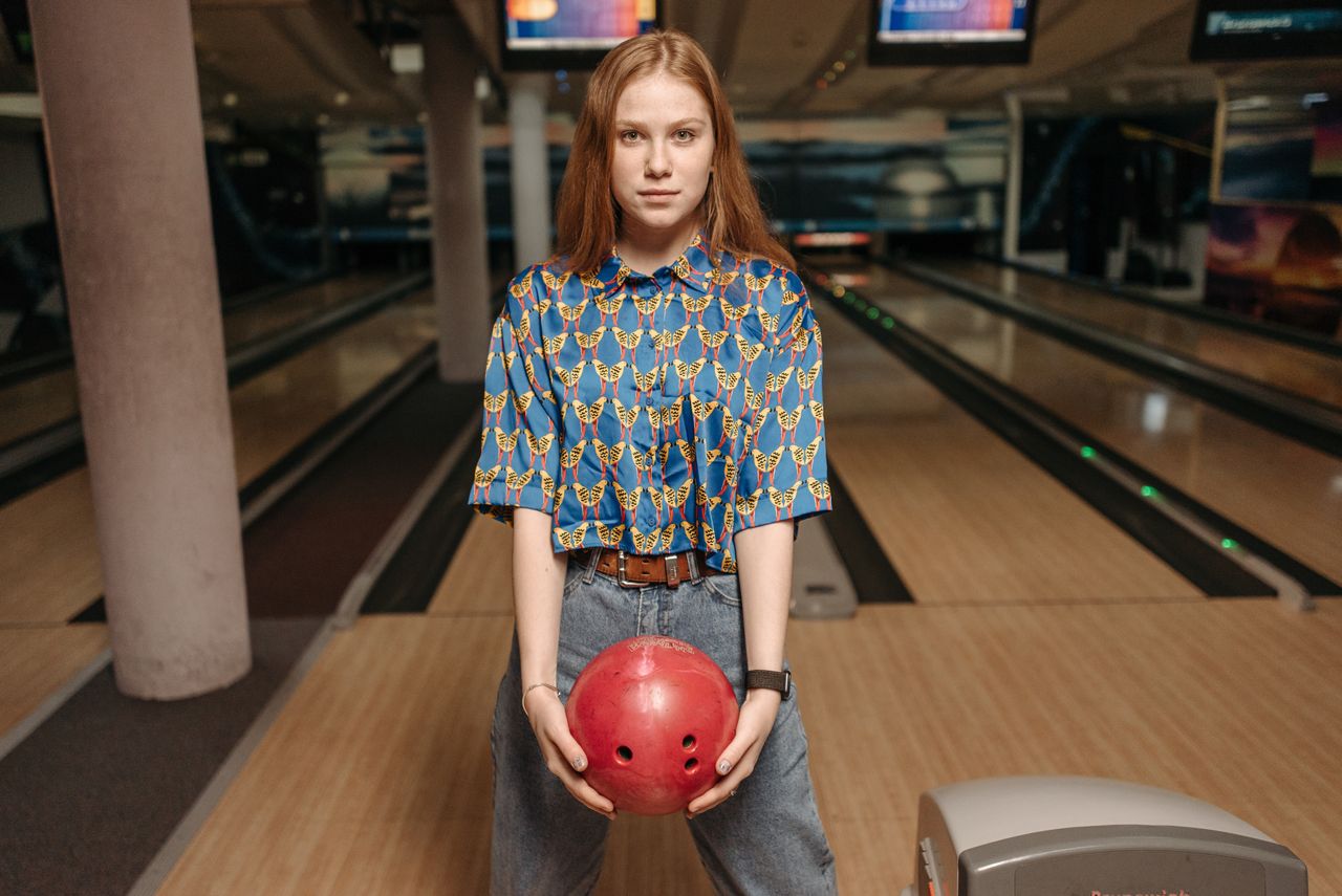 Young woman in a colorful shirt holding a bowling ball at an indoor bowling alley.